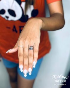 a woman with a small bow tattoo on her ring finger, wearing blue shorts and an orange t - shirt