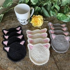 crocheted cat mittens and coffee mug cozyies on a table with flowers