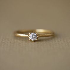 a gold ring with a single diamond on it sitting on a beige tableclothed surface