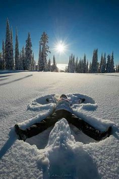 a person laying in the snow with their legs spread out to look at the sun