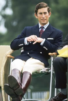 a man in a suit and tie sitting on a chair with his legs crossed, wearing brown boots