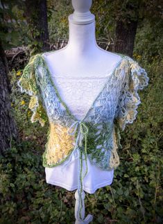 a white mannequin with green and yellow crocheted shawl on it