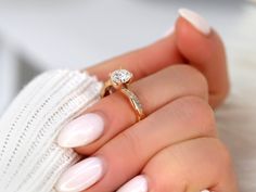 a woman's hand holding a ring with a diamond on it and white manicured nails