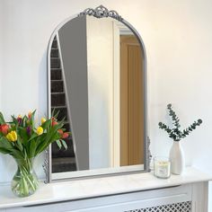 a vase filled with flowers sitting on top of a white mantle next to a mirror