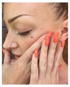 a woman with bright orange nail polish holding her hand to her face and looking at the camera