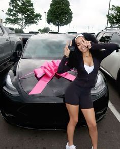 a woman standing in front of a car holding a pink ribbon