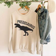 a dinosaur sweatshirt hanging on a rack next to a pair of denim jackets and jeans