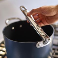 a person holding a pair of tongs over a pot on the stove