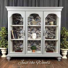 a white china cabinet with black and white wallpaper on the walls, along with potted plants