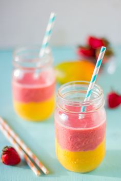 two mason jars filled with smoothie and strawberries on a blue table next to strawberries