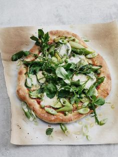 a pizza topped with green vegetables on top of parchment paper