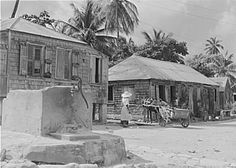 an old black and white photo of people in front of shacks on the street