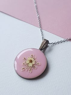 a pink necklace with a flower on the front and back of it, hanging from a silver chain