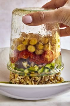 a person touching the top of a layered salad in a glass jar on a white plate