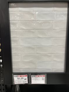 a white brick wall mounted to the side of a store display case with price tags on it