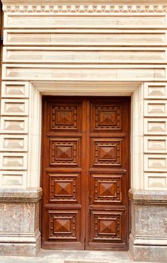 two large wooden doors on the side of a building with stone pillars and columns in front of them