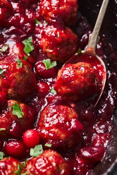 meatballs and cranberry sauce in a black skillet with a wooden spoon