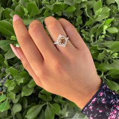 a woman's hand with a diamond ring on her finger and green leaves in the background