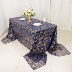 a table covered in blue and gold cloths next to a vase with white flowers