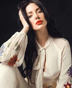 a woman with long black hair and red lipstick posing for a photo in front of a black background