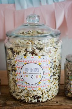 a glass jar filled with popcorn sitting on top of a wooden table next to other items