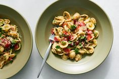 two bowls filled with pasta and veggies on top of a white tablecloth