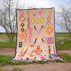 a large multicolored rug sitting on top of a dirt field next to trees