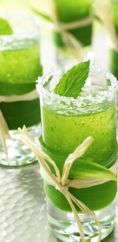 four glasses filled with green drinks and garnished with leaves