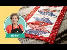 a woman with an apron on standing next to a quilted table runner that has the name jenny written on it