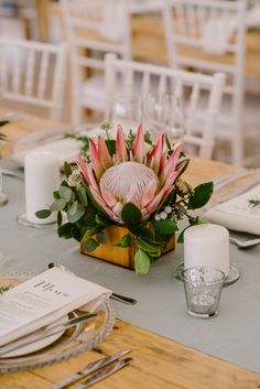 an arrangement of flowers and greenery sits on a table at a wedding reception with place settings