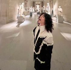 a woman standing in a room with statues on the wall behind her and looking up into the sky