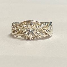 a white gold ring with an intricate design on the front and center, sitting on a table