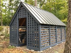 a large wooden shed sitting next to a tree in the middle of a forest with lots of leaves on the ground