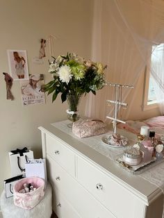 a white dresser sitting next to a window filled with flowers and other items on top of it