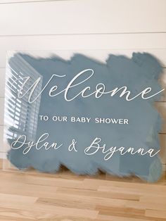 a welcome sign for a baby shower is displayed on a wooden floor in front of a white wall