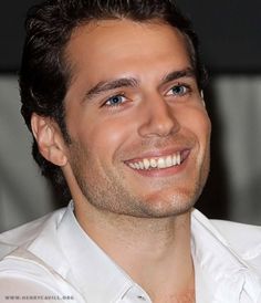 a close up of a person wearing a white shirt and smiling at the camera with his eyes wide open