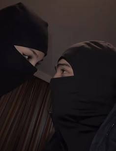 two people in black headscarves facing each other with their eyes closed and one wearing a hood