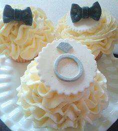 three cupcakes on a plate decorated with bows and diaper clips, one has a ring