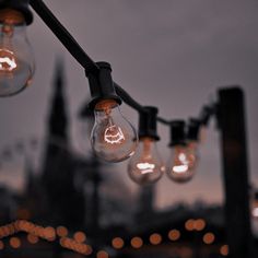 several light bulbs are hanging from a black pole with lights in the dark behind them