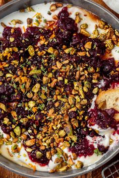 a pan filled with fruit and nuts on top of a wooden table next to bread