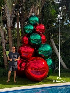 a man standing in front of a giant christmas tree made out of shiny red and green balls