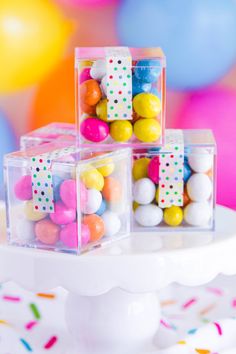 three clear boxes filled with colorful candies on top of a white cake platter