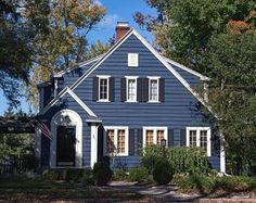 a blue house with black shutters and white trim on the front door is surrounded by trees