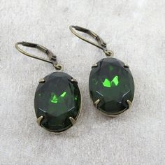 "Vintage European glass jewels are featured in these beautiful earrings. Jewel color is lovely turmaline green in an 18x13mm oval shape. Turmaline green is no ordinary green. It is a stunning rich green reminiscent of fern green. These gorgeous jewels have a wonderful glow when the light hits them. They have been hand set into antiqued brass settings and dangle from matching lever back ear wires. Total measurement is 1.5\". All items come gift boxed in my signature gift wrapping and ready to giv Green Oval Earrings For Party, Ornate Green Earrings For Gift, Victorian Green Earrings, Luxury Green Vintage Earrings, Howls Moving Castle Earrings, Luxury Green Gemstone Earrings, Green Oval Nickel-free Earrings, Victorian Gothic Jewelry, Luxury Green Vintage Clip-on Earrings