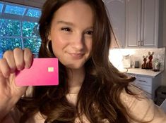 a woman holding up a pink card in front of her face and looking at the camera