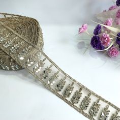 a roll of silver sequined ribbon next to pink flowers and purple carnations