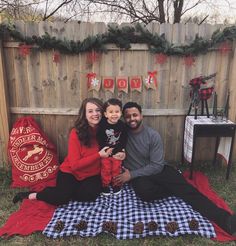 a man, woman and child sitting on a blanket in front of a fence