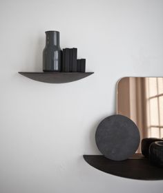 a mirror and some shelves on the wall in a room with white walls, black vases and other items