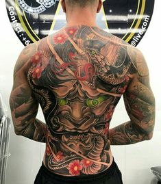 a man with tattoos on his back standing in front of a mirror