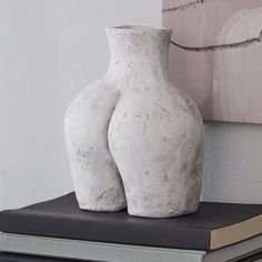 two white vases sitting on top of a book next to a pink and gray painting